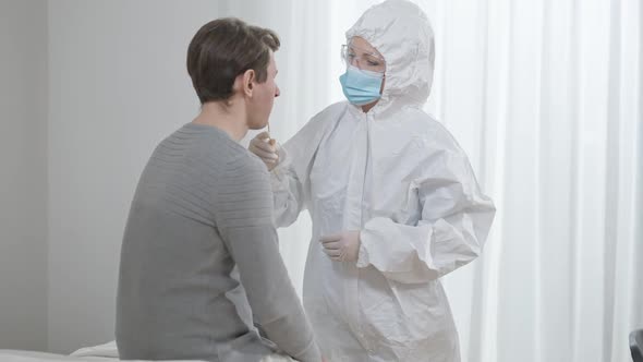 Doctor or Nurse in Face Mask and Protective Suit Taking Covid Test in Hospital