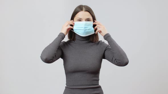 Caucasian Woman In Gray Turtle Neck Dress On A Grey Background Put A Face Mask On