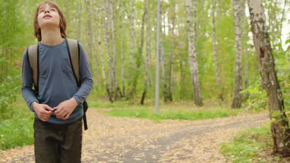 Boy Teenager with Backpack Walking on Autumn Park on Green Trees Background