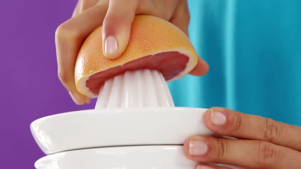 Woman preparing blood orange juice from juicer against violet background