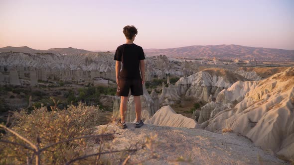 Young man stands on mountain top overlooking view and sunset