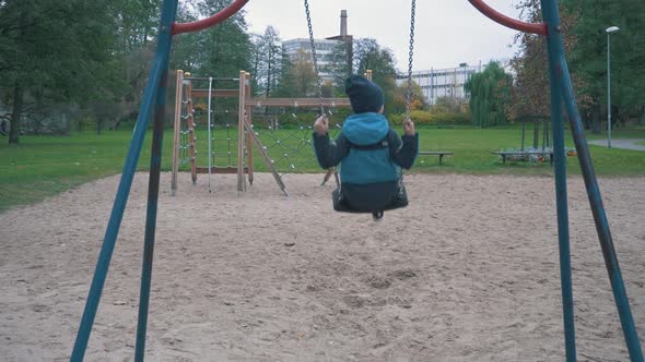 Boy is Swaying on Swing in Park at Autumn Day and Jumping Out in Slow Motion