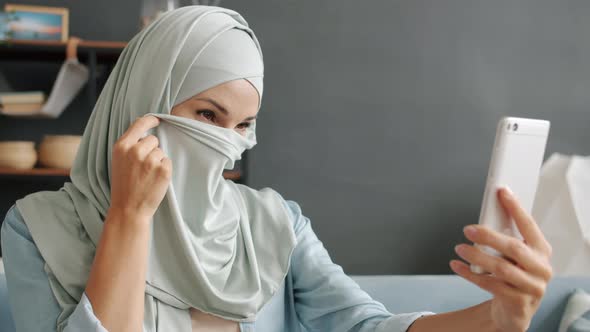 Slow Motion Portrait of Cheerful Muslim Lady Posing for Smartphone Camera Taking Selfie Indoors