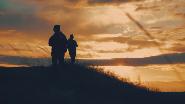 Silhouettes of Two Hikers with Backpacks Enjoying Sunset View From Top of a Mountain. Enjoying the