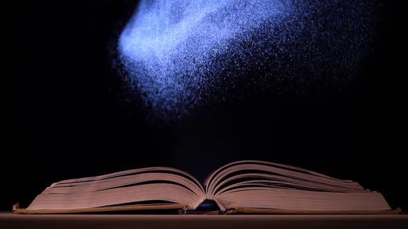 A Beam of Light Illuminates the Pages of an Open Book on a Table in a Dark Studio