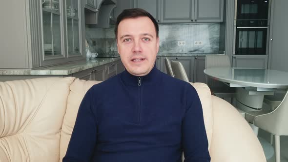 Young adult man sitting on sofa at home and looking at camera