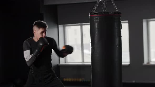 Athletic Young Man Boxer Wearing Sports Clothes Hitting the Punching Bag in the Gym