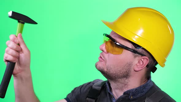 The Builder Works with a Hammer on the Background of a Chroma Key in the Studio