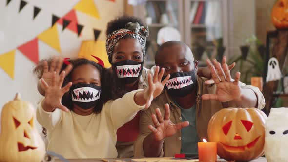 Cheerful Black Family in Halloween Masks Scaring the Camera at Home