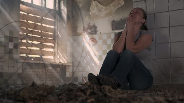 Depressed woman crying while sitting on floor in abandoned building alone