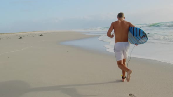 Male surfer running on the beach 4k