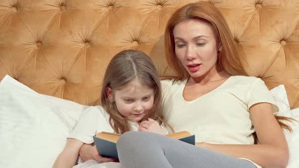 Little Girl and Her Mom Smiling To the Camera Reading a Book