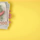 The hand of a young woman holds a lot of dollar bills on a bright yellow background copy space - VideoHive Item for Sale