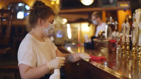 Young Waitress in Safety Mask Wiping Bar Counter with Duster and Detergent