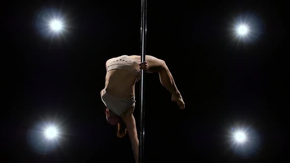 Acrobatic Movement on the Pole Is Performed By a Girl. Black Background, Slow Motion, Back Lanterns