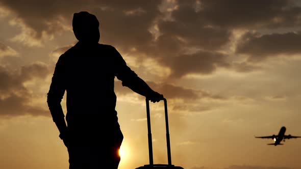 Silhouette of a Tourist with Luggage at Sunset at the Airport