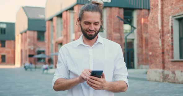 Man Looking to Camera Holding Smartphone in His Hand Standing at City Street.