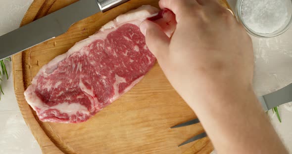 A Man's Hand Puts a Striploin Steak on a Cutting Board. 