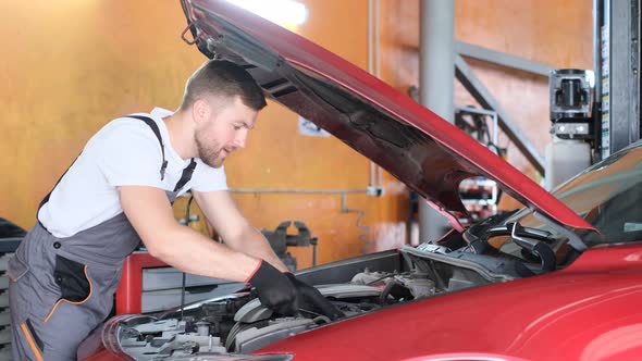 A Handsome Professional Car Service Mechanic Repairs a Car Engine