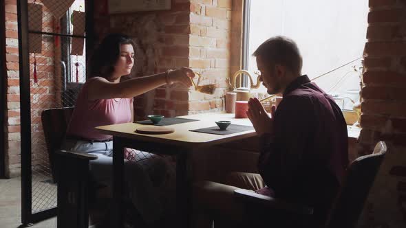 Side View of Young Happy Boyfriend and Girlfriend Chatting During Breakfast with Cups of Tea Sitting