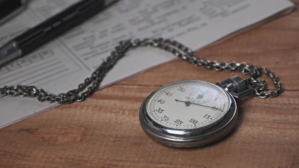 Antique Stopwatch Lies on Wooden Desk with Old Documents and Counts Seconds