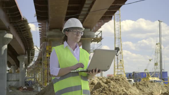 Female foreman working on laptop at bridge construction site