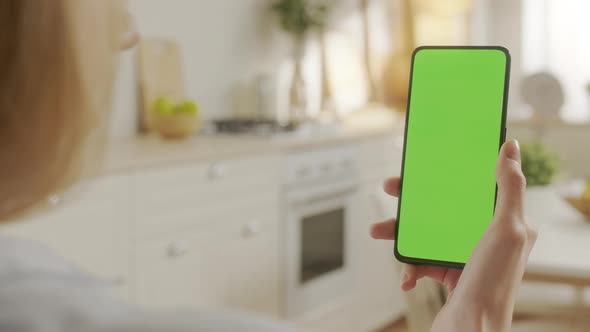 Back View of Woman at Kitchen Room Using Phone With Green Mockup Screen Chroma Key Without Track