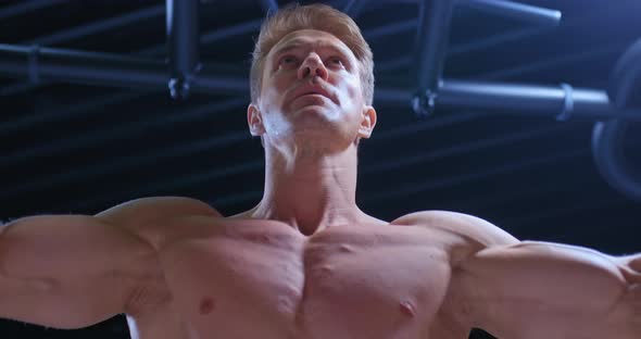 Portrait of a Young Muscular Bodybuilder Doing Convergence of Hands on the Upper Block Strength