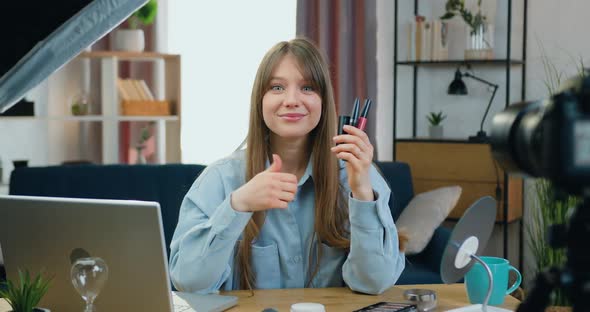 Beauty Blogger Holding Cosmetics Products in One Hand Another Gesturing Alright into Camera