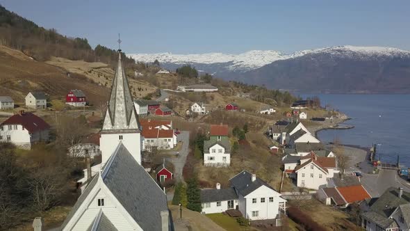 Aerial Shot Orbiting Around a Church Steeple in a Norwegian Village with Snow Capped Mountains and a