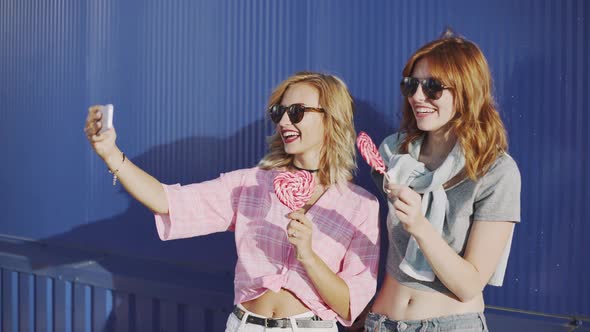 Two Young Attractive Women Walking and Talking on Street and Eat Lollipop