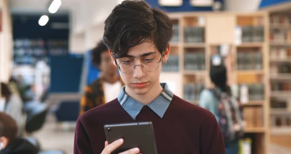 Male College Student Using Digital Tablet Standing in Library