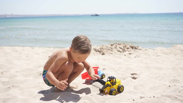 on a Sunny Hot Summer Day, a Boy Plays with Sand and Toys, Cars on the Beach. A Child Plays Sitting