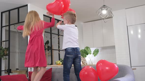 Little Boy and Girl Dancing with Red Heart Shape Balloons at Home