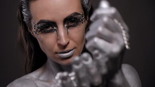 Woman with Silver Paint on Her Skin Face and Hair Poses in a Studio with Chain