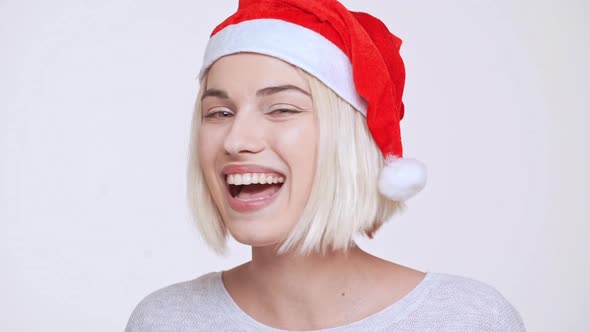 Young Beautiful Blonde Girl in Christmas Hat Smiling Winking Sending Kisses Ovwer White Background