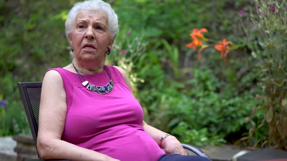Elderly woman has a face of amazement and shock while sitting outside in a garden area.