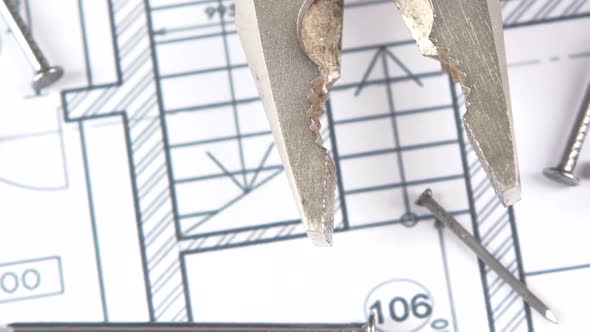 Gray and Red Pliers on Building Plan, Scheme Among Nails, Rotation, Close Up