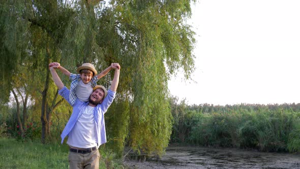 Father and Son in Straw Hats Are Playing and Fooling Around on Open Air in Countryside