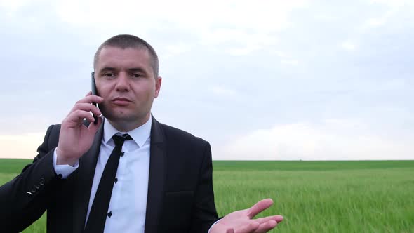 A Man in a Business Suit is Talking on a Smartphone in the Middle of the Field