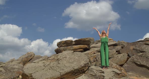 Pretty Woman in Green Dress is Doing Yoga on a Rocky Shore Sunny