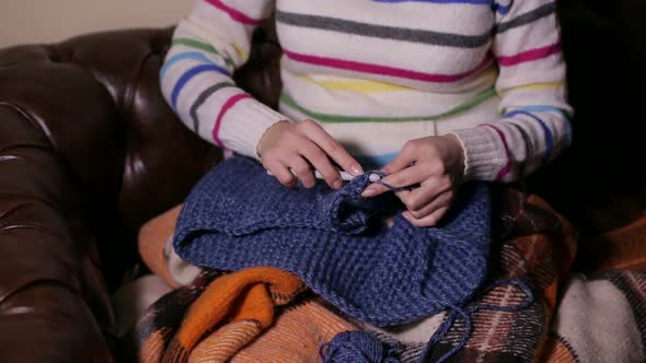 Beautiful Girl Sitting on the Couch with Blanket and Knitting a Scarf