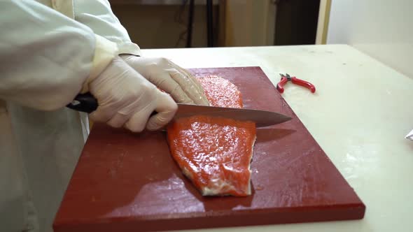 White coated fish industry worker cutting a salmon filet in two pieces - slow motion static shot fro