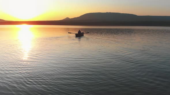 Man Sailing on the Boat with Paddles on the River While the Sunset