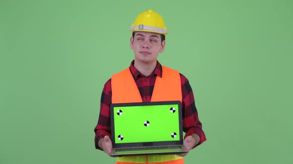 Happy Young Multi Ethnic Man Construction Worker Thinking While Showing Laptop