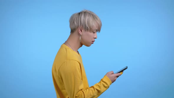Handsome Asian Man Using Smartphone on Blue Studio Wall