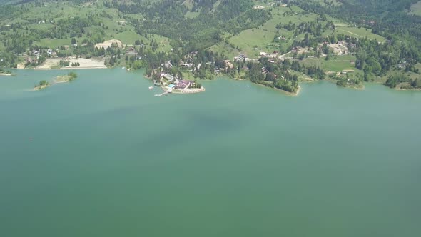 Aerial Apprpach shot of Lake with Green Forests on a sunny day