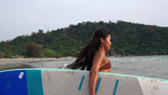 Beautiful Young Woman In Bikini Carrying Paddleboard To Sea