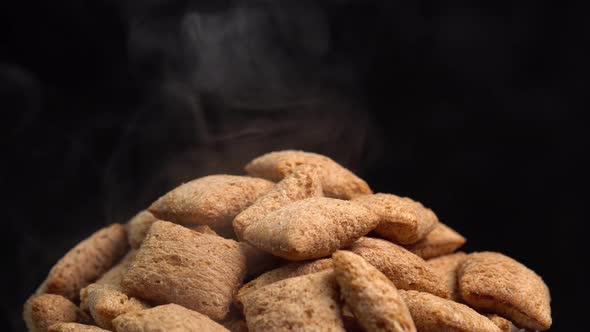 Hot crispy chocolate pads rotation with smoke in macro on black background. Cereal dessert