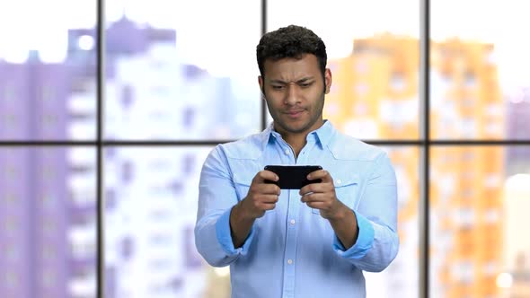 Expressive Young Darkskinned Man Plays Smartphone Game
